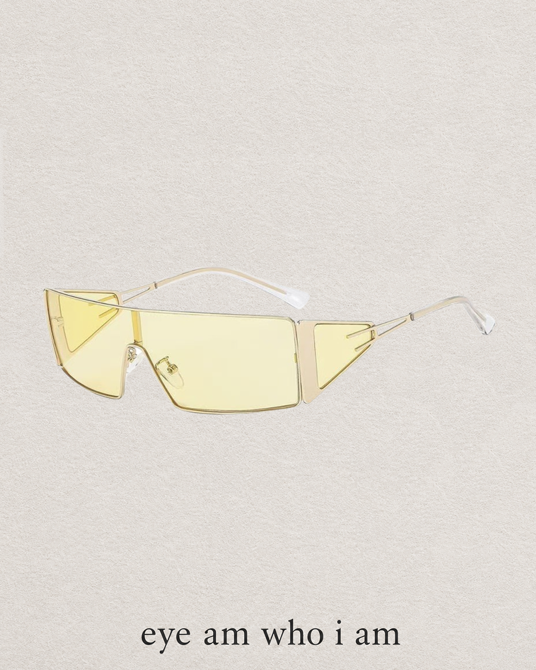 A pair of geometric rimless sunglasses with pale yellow tinted lenses and a gold-tone frame, displayed on a textured light beige background with the text 'eye am who i am' underneath.